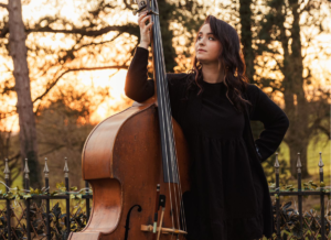 Jess standing next to the double bass in a woodland setting.
